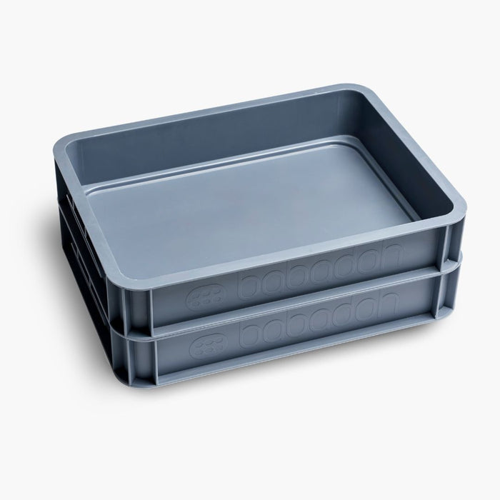 A side-on view of two empty steel-blue dough trays with a smooth, glossy surface, slightly raised edges and the words 'Babadoh' along the side.
