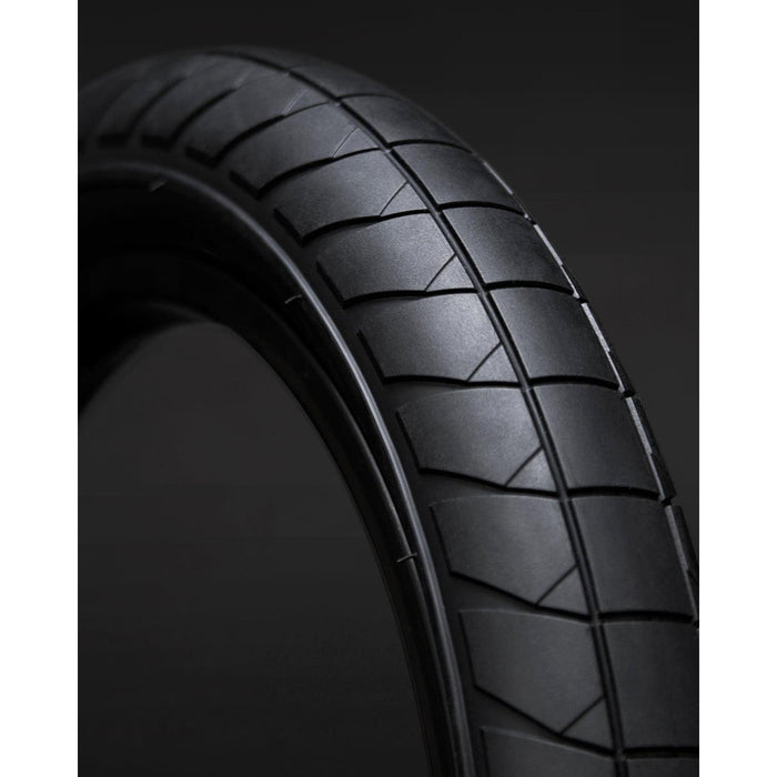 Close-up of a Fly Bikes Fuego 20 Inch Tyre in black, featuring a textured tread pattern and engineered for high-pressure puncture resistance, set against a dark background.