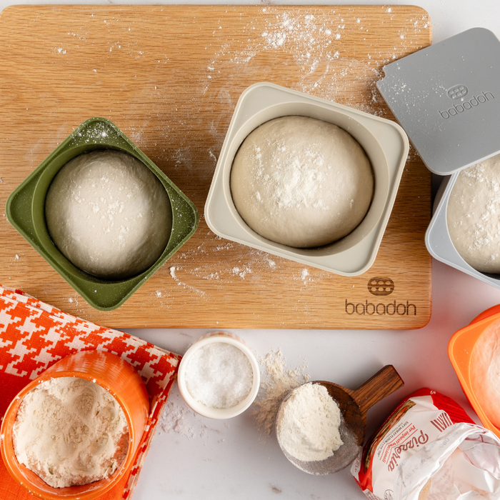 A top down view of Babadoh containers holding proved pizza dough balls, sitting on top of an oak cutting board.